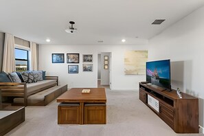 A modern living room with a wooden coffee table, a sofa with cushions, a television on a wooden stand, and framed pictures on the wall. - Luxury 6BR Villa w/ Pool, Spa & Near Disney (Kissimmee)