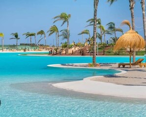 A resort pool area with clear blue water, palm trees, and a thatched umbrella. - The Marina Oasis - Santa Rosalia Lake Resort (Torre-Pacheco)