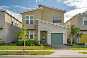A modern two-story residential building with a stone facade, a green garage door, and a well-maintained lawn. - 5BR Villa w/ Pool & Game Room Near Disney (Davenport)
