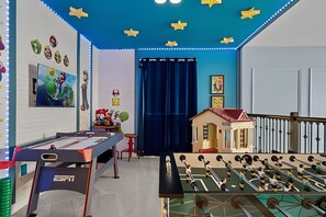 A room with a foosball table, a small house model, and various wall decorations including a Mario-themed painting. - 5BR Villa w/ Pool & Game Room Near Disney (Davenport)