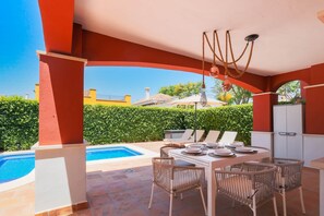 Um pátio externo com piscina, mesa de jantar, cadeiras e luminária pendente.