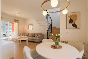 A modern living room with a sofa, coffee table, and a dining table with a vase of flowers. - Villa James - Mar Menor Golf Resort (Torre-Pacheco)