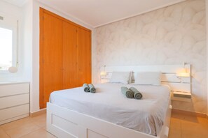 Quarto com cama, guarda-roupa de madeira, mesas de cabeceira brancas e parede estampada.