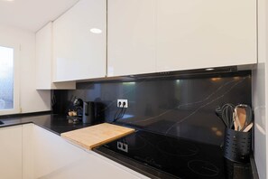 A modern kitchen with white cabinets, a black stovetop, and a wooden cutting board. - Villa James - Mar Menor Golf Resort (Torre-Pacheco)