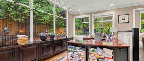 A modern kitchen with dark wood cabinets, a wooden floor, and large windows offering a view of greenery.