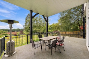 En udendørs terrasse med et bord, stole, varmelegeme og udsigt til en anlagt have.