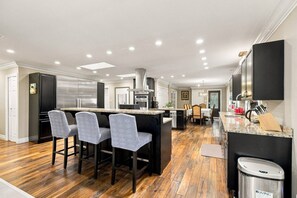Een moderne keuken met een centraal eiland, barkrukken en een eethoek met een tafel en stoelen.