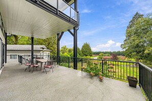 Un patio cubierto con mobiliario exterior, vistas a un jardín ajardinado y un edificio al fondo.
