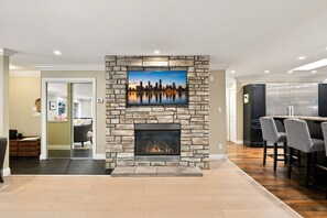 Una sala de estar moderna con chimenea de piedra, un televisor de pantalla plana montado encima y una zona de comedor con taburetes de bar.