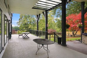 Een overdekt terras buiten, met een tafel en stoelen, omringd door een balustrade en bomen.