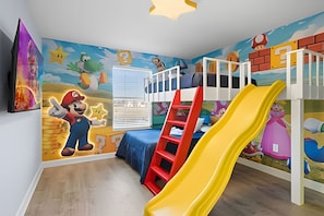 A child's playroom with a bunk bed, a yellow slide, and Mario-themed wall art. - 4BR w/ Mickey & Mario Rooms + Heated Pool (Davenport)
