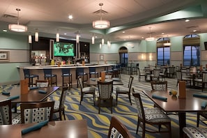A hotel dining area with multiple tables and chairs, a bar, and a television screen displaying a program. - 4BR w/ Mickey & Mario Rooms + Heated Pool (Davenport)