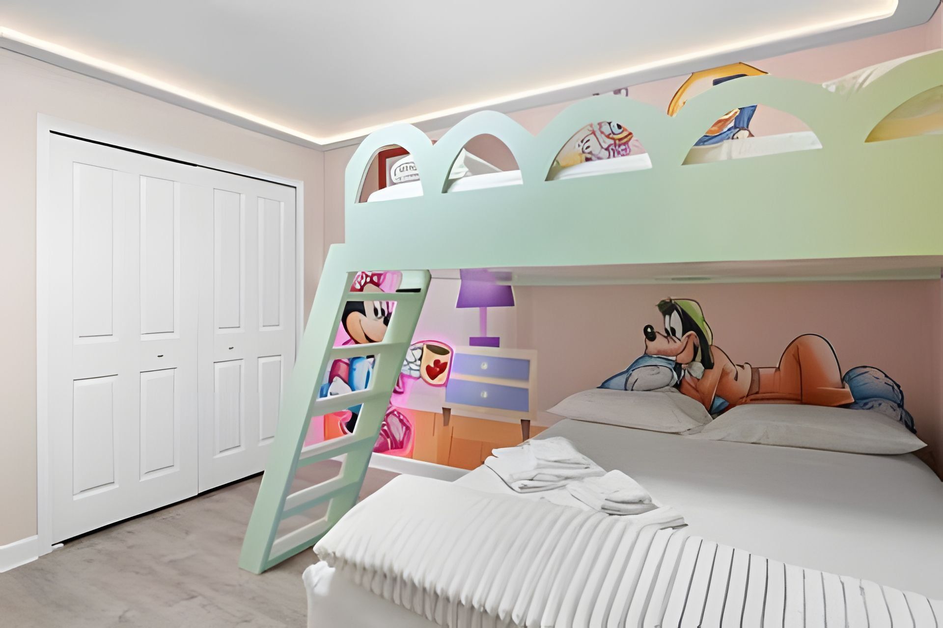A bunk bed with cartoon character decorations, a white wardrobe, and a bedside table with a lamp.