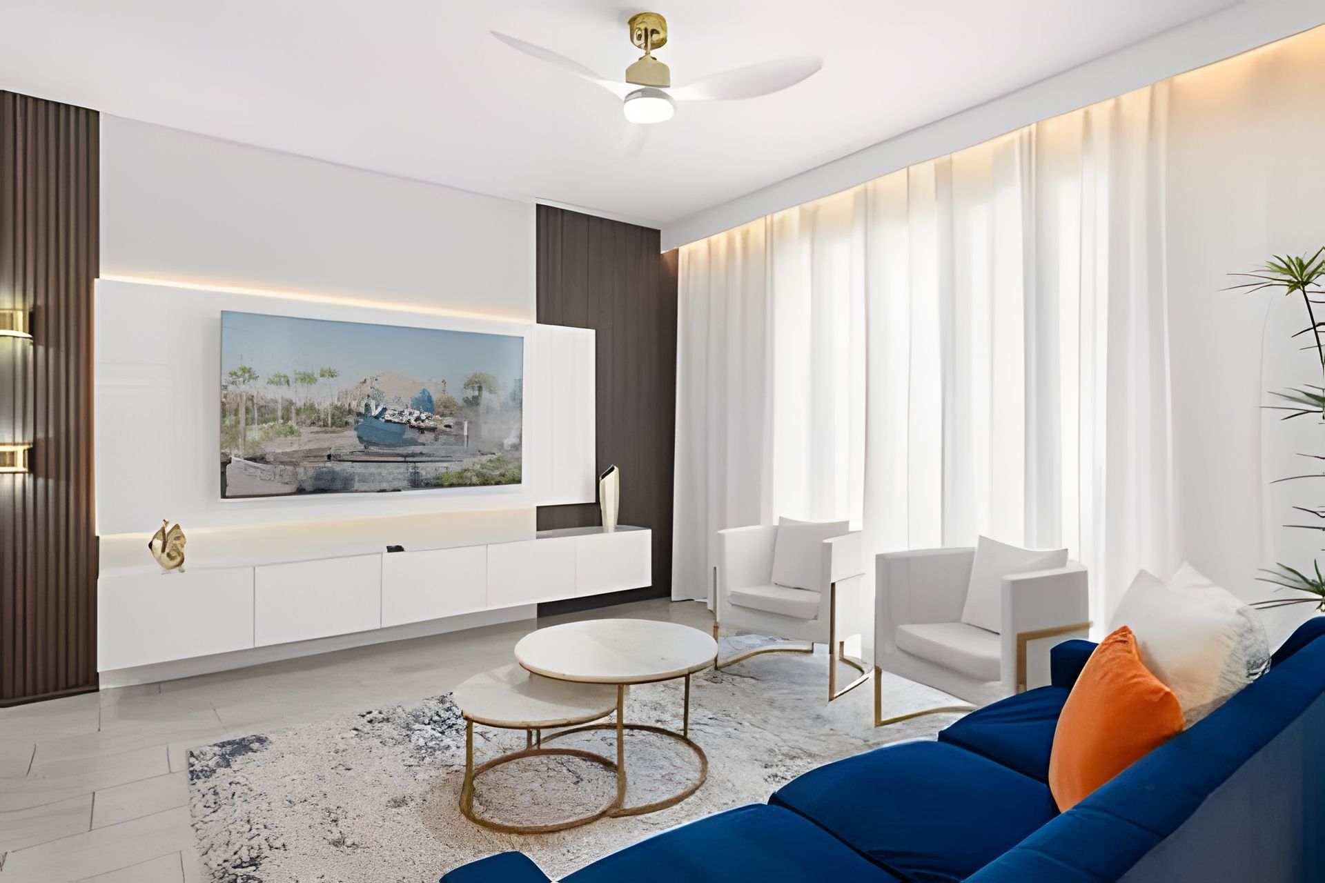 A modern living room with a large flat-screen TV mounted on the wall, white sofas, a coffee table, and a ceiling fan.