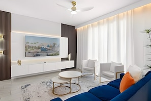 A modern living room with a large flat-screen TV mounted on the wall, white sofas, a coffee table, and a ceiling fan. - 4BR w/ Mickey & Mario Rooms + Heated Pool (Davenport)