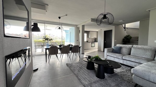 Un salon moderne avec un canapé gris, un coin repas comprenant des chaises et une table, et une cuisine en arrière-plan.