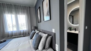 A modern bedroom with a large bed, a bedside table, a lamp, and a bathroom with a mirror and sink. - Villa Oliver - Mar Menor Golf Resort (Torre-Pacheco)