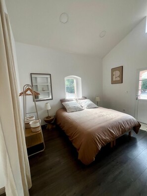 A bedroom with a bed, a bedside table, a lamp, a window, and a door. - New Listing (Montauban)