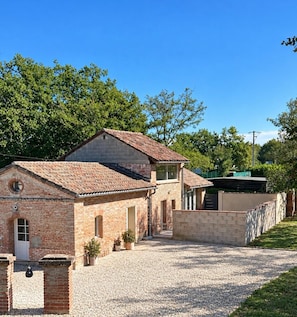 A two-story brick building with a tiled roof, a gravel driveway, and a small garden area with potted plants. - New Listing (Montauban)