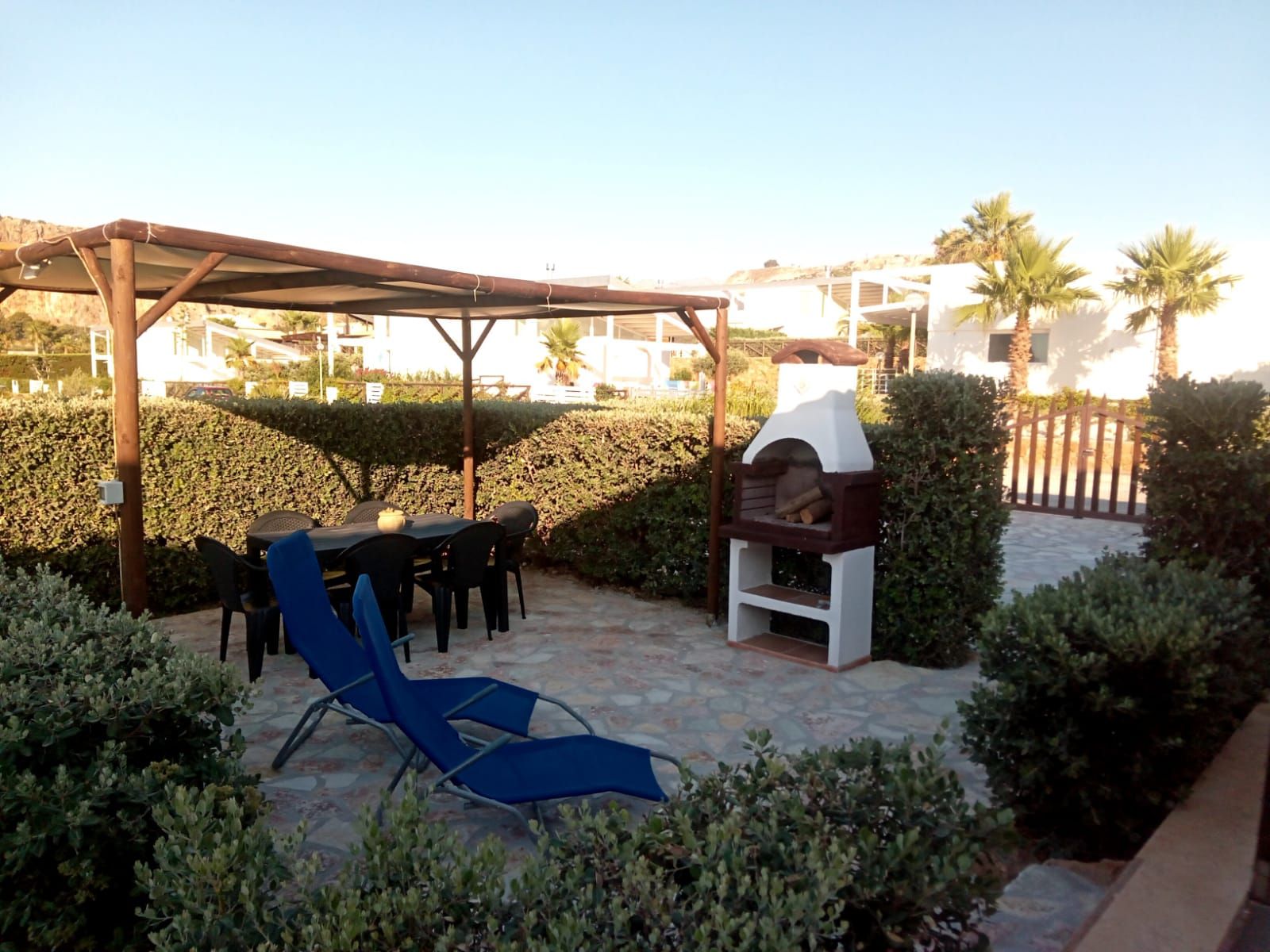 Une terrasse extérieure équipée d’un barbecue, d’un espace salon couvert et d’un fauteuil de détente.