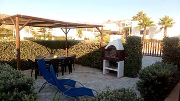 Une terrasse extérieure équipée d’un barbecue, d’un espace salon couvert et d’un fauteuil de détente.