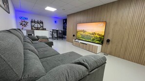 A modern living room with a large flat-screen TV, grey sofas, a wooden accent wall, and a neon sign. - 7LakesVilla - Santa Rosalia Lake Resort (Torre-Pacheco)