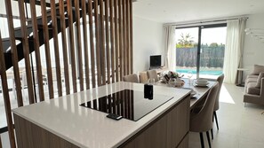 A modern kitchen with a central island, dining area, and a view of a swimming pool. - 7LakesVilla - Santa Rosalia Lake Resort (Torre-Pacheco)