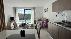 A modern kitchen with a built-in dishwasher, a dining area with a table set for two, and a large sliding glass door leading to a pool. - 7LakesVilla - Santa Rosalia Lake Resort (Torre-Pacheco)