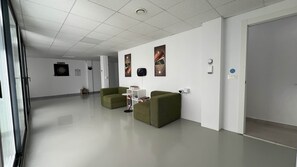 A hallway with two green sofas, a white shelf with books, and a dartboard on the wall. - 7LakesVilla - Santa Rosalia Lake Resort (Torre-Pacheco)