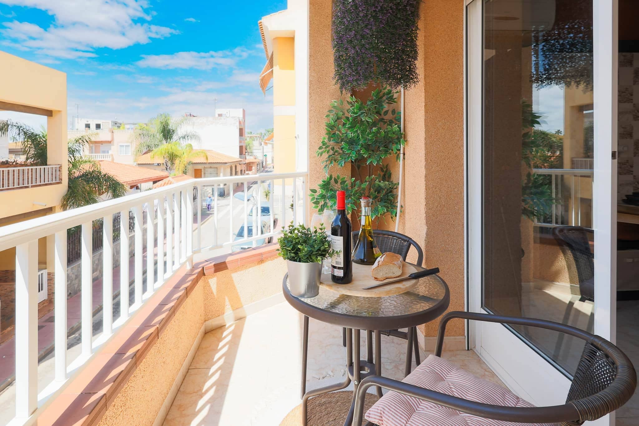 Ein Balkon mit Tisch, Stühlen, einer Weinflasche und einem Blumentopf.