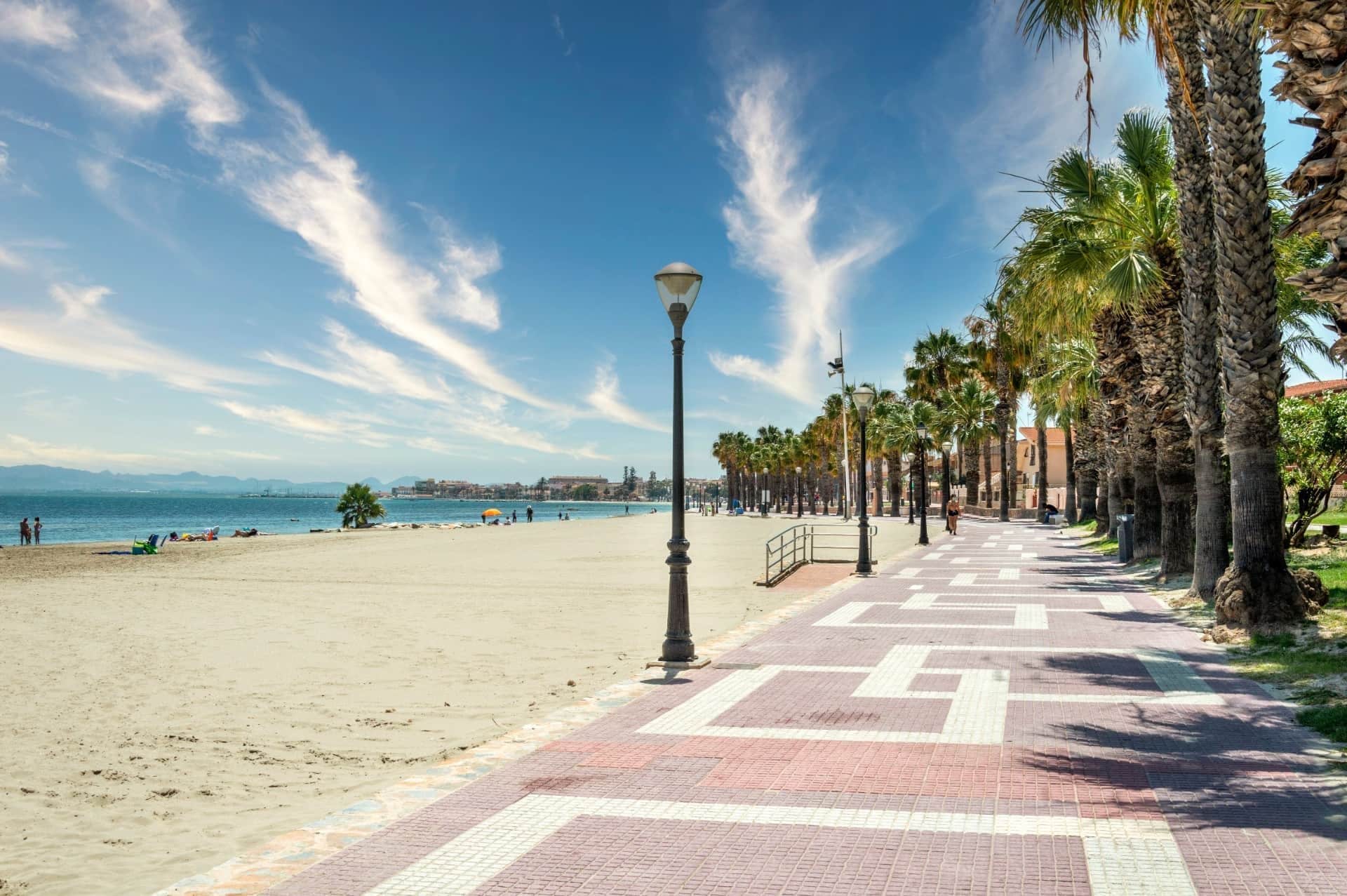 Une promenade en bord de mer, avec un sentier pavé, des palmiers et une vue dégagée sur la mer.