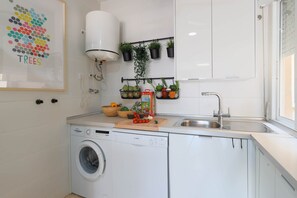 Eine kleine Küche mit Waschmaschine, Spüle und einer Arbeitsplatte, auf der ein Schneidebrett und Gemüse liegen.