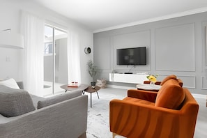 A modern living room with a sofa, a coffee table, and a TV mounted on the wall. - 4BR w/ Pool + Mickey & Star Wars Rooms (Davenport)
