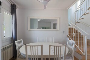 A dining area with a round table and chairs, a ceiling fan, a window with curtains, and a staircase with a railing. - Casa Sol - Mar Menor Golf (Torre-Pacheco)