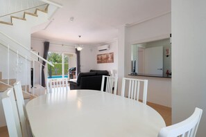Ett modernt vardagsrum med ett vitt matbord, en svart soffa och en trappa som leder upp till ett övre våningsplan.