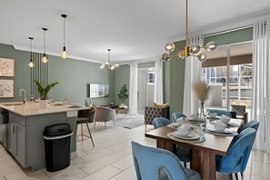 A modern kitchen with a central island, dining area with blue chairs, and a large window providing natural light. - Disney-area 4BR Townhome w/ Heated Pool (Davenport)