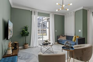 A living room with a sofa, armchairs, a coffee table, a TV, and a plant. - Disney-area 4BR Townhome w/ Heated Pool (Davenport)