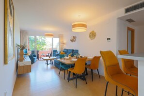 A modern dining area with a wooden table and orange chairs, a blue sofa, and a ceiling light fixture. - La Casa Soleada - Mar Menor Golf Resort (Torre-Pacheco)