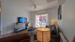 Ein modernes Wohnzimmer mit Flachbildfernseher, Sofa, Couchtisch und einer Lampe.