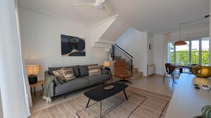 Ein modernes Wohnzimmer mit einem grauen Sofa, einem schwarzen Couchtisch und einer Treppe, die zu einer oberen Etage führt.