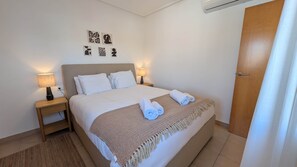 Ein ordentlich bezogenes Bett mit einem gemusterten Überwurf, zwei Nachttischlampen und Bildern an der Wand.
