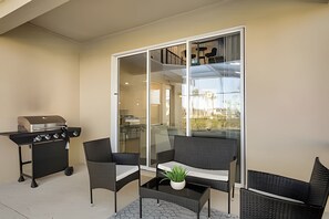 A balcony with a grill, two chairs, a small table with a plant, and a view of the interior through a glass door. - 5BR Villa w/ Pool, Game Room + Themes Near Disney (Kissimmee)