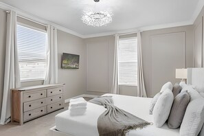 A bedroom with a bed, a dresser, and a chandelier. - 5BR Villa w/ Pool, Game Room + Themes Near Disney (Kissimmee)