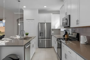 A modern kitchen with stainless steel appliances, white cabinetry, and a central island. - 5BR Villa w/ Pool, Game Room + Themes Near Disney (Kissimmee)