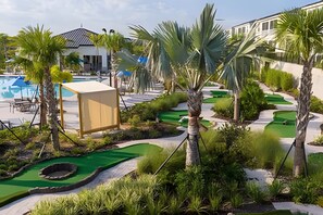 Un terrain de golf avec une piscine, des palmiers et un bâtiment en arrière-plan.