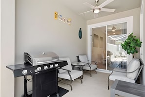 A modern patio area with a built-in grill, white chairs, and a ceiling fan. - Championsgate 4BR w/ Pool, Themes, Near Disney (Davenport)