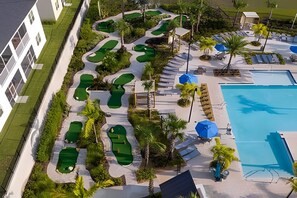 An aerial view of a resort with multiple green golf courses, a large swimming pool, and sun loungers. - Championsgate 4BR w/ Pool, Themes, Near Disney (Davenport)