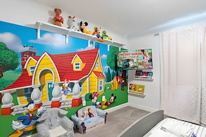 Une chambre d’enfant avec une fresque représentant une ferme, des étagères remplies de jouets et un livre intitulé « Mausy la souris ».