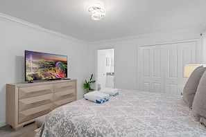 Une chambre à coucher avec un lit, une commode, un téléviseur et une porte.