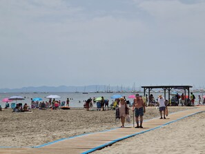 Ein Strand mit einem hölzernen Promenadenweg, Menschen und Booten in der Ferne.